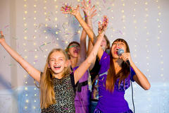 Bild vergrern: Group of happy girls with headphones singing together on karaoke on background of lights