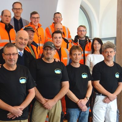 Bild vergr&ouml;&szlig;ern: Landrat Eberhard Nu&szlig; (2. Reihe, links) freut sich mit den Mitarbeitern der Stra&szlig;enmeistereien sowie dem Multifunktionsdienst des Landratsamtes &uuml;ber deren fair gehandelte Arbeitskleidung, die jetzt um T-Shirts erweitert wurde. Initiiert wurde die Beschaffung f&uuml;r den Multifunktionsdienst vom Leiter der Kreisentwicklung, Michael Dr&ouml;se (ganz hinten) sowie seiner Mitarbeiterin Brigitte Schmid (2. Reihe, rechts).