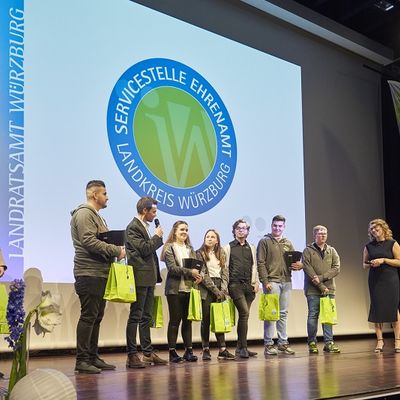 Eine Gruppe ehrenamtliche Mitglieder, die von Kerstin Gressel eine Dankesurkunde erhalten haben, stehen auf der B&uuml;hne.