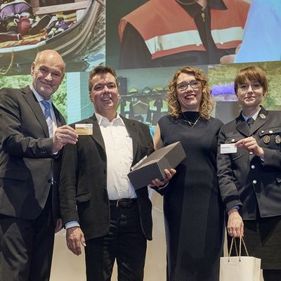 Landrat Eberhard Nu&szlig; steht zusammen mit zwei geehrten Ehrenamtsmitgliedern und einer Mitarbeiterin des Landratsamts auf der B&uuml;hne und h&auml;lt eine goldene Karte in der Hand.