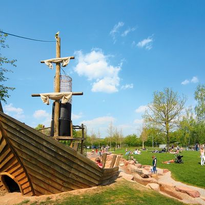 Ein h&ouml;lzernes Piratenschiff, das umgeben von Sand und Wiesen auf einem Spielplatz ist.