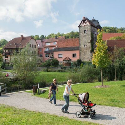 Eine Familie, die auf einem Weg mit B&auml;umen und Gr&uuml;nfl&auml;chen vor den Toren der Gemeinde spazieren geht.