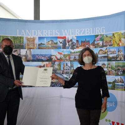 Landrat Thomas Eberth &uuml;berreicht Kerstin Celina die Kommunale Dankurkunde des Bayerischen Innenministers. Beide tragen FFP2-Maske.