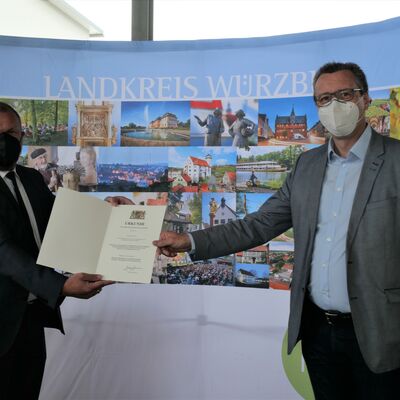 Landrat Thomas Eberth überreicht Bürgermeister Jürgen Götz die Kommunale Dankurkunde des Bayerischen Innenministers. Beide tragen FFP2-Maske.