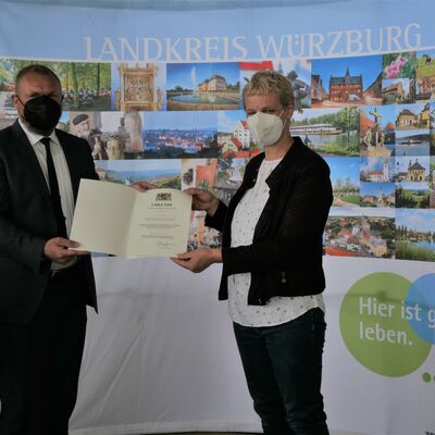 Landrat Thomas Eberth &uuml;berreicht Lioba Kinzinger die Kommunale Dankurkunde des Bayerischen Innenministers. Beide tragen FFP2-Maske.