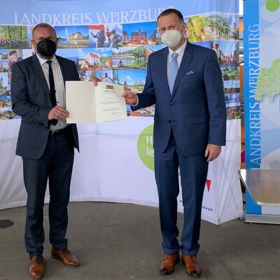 Landrat Thomas Eberth &uuml;berreicht B&uuml;rgermeister Johannes Menth die Kommunale Dankurkunde des Bayerischen Innenministers. Beide tragen FFP2-Maske.