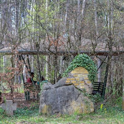 Rastplatz Siebenertisch, welcher aus einem Pavillon und einem von Efeu bewachsenem Stein besteht und in einem Wald liegt.