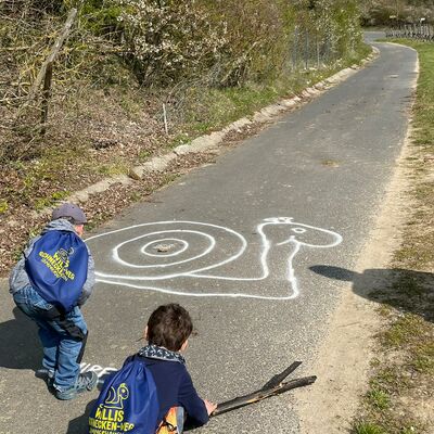 Zwei Kinder malen mit Kreide Schnecken auf den Weg.