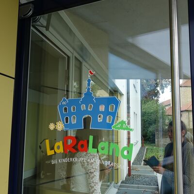 Eine gl&auml;serne T&uuml;r auf der ein blaues Abbild des Landratsamtes gedruckt ist. Es steht der Schriftzug LaRaLannd darunter.