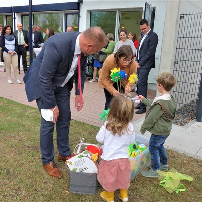 Landrat Thomas Eberth und Isabell Schumacher vom B&uuml;ro des Landrats &uuml;berreichen zwei Kindern Windr&auml;der zum spielen.