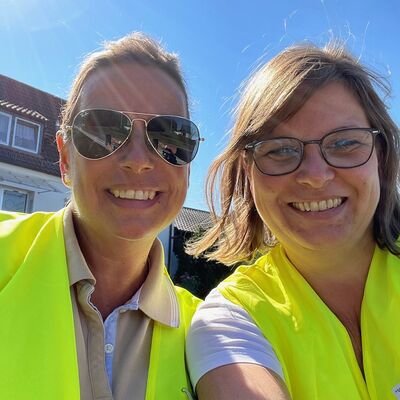 Zwei Frauen mit Warnwesten stehen lachend nebeneinander.