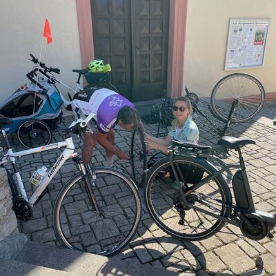 Zwei Fahrradfahrer reparieren einen Fahrradreifen vor einer Kirche.