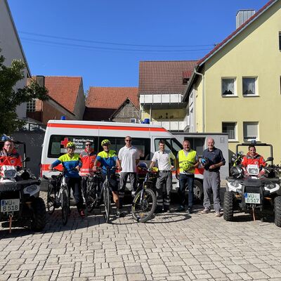 Mehrere Fahrradfahrer stehen vor einem Rettungswagen.