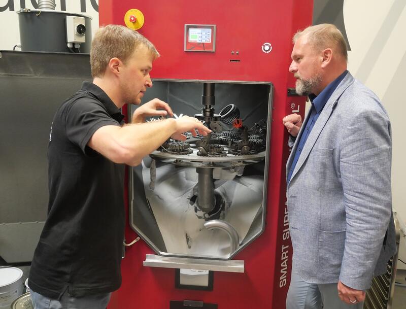 Bild vergrößern: Geschäftsführer Christian Staudigel (links) erklärt Landrat Thomas Eberth (rechts) vor der geöffneten Maschine den abschließenden Prozess der Oberflächenbehandlung der fertig gedruckten Metallteile.